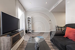 Living room with black velvet sofa, flat TV on a cabinet in front