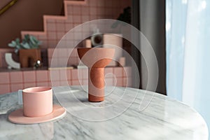 Living room corner decorated with clay ceramic vase and baby pink cup on white marble  table with pink tile stair in the