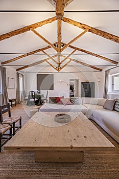 Living room of a country house with wooden and metal trusses on the roof, vintage-style wooden furniture and a large curved sofa