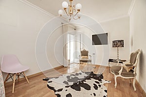 a living room with cowhide floor, corner lamp, golden ceiling lamp with five lampshades and Louis XV style chairs