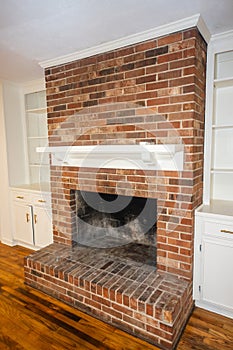 A living room or den with hardwood floors, white walls and a red brick fireplace with mantle in a newly renovated house