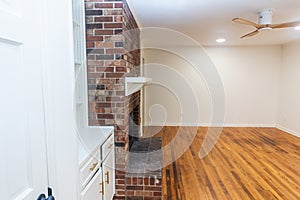 A living room or den with hardwood floors, white walls and a red brick fireplace with mantle in a newly renovated house