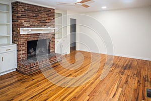 A living room or den with hardwood floors, white walls and a red brick fireplace with mantle in a newly renovated house