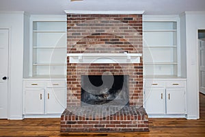 A living room or den with hardwood floors, white walls and a red brick fireplace with mantle in a newly renovated house