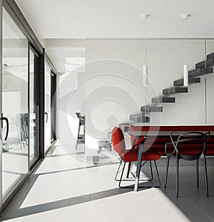 Living room detail with poltra and red sofa, cantilevered staircase, and there are stools at the bottom