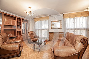 Living room of a house with oak parquet floors with wooden and brown leather tresillo and matching wooden bookcase