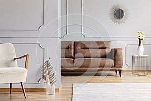 Living room interior with decorative mirror on wall with wainscoting, brown leather sofa, fresh roses on end table and photo