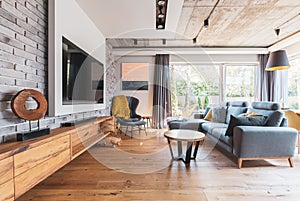 living room with light wooden floor, grey couch and wing back chair and big tv on the wall