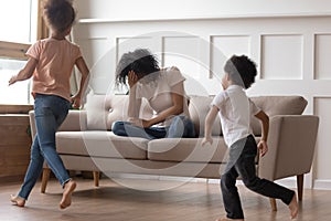 African mother sit on couch can`t handle with noisy kids photo