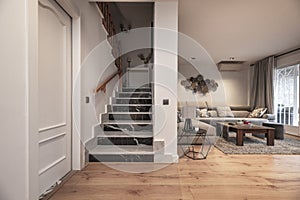 Living room with pine wood floors, marble stairs, dark wood coffee table, gray corner sofa and exit to terrace