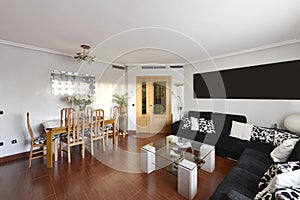 Living room of a residential home with a wooden dining table with matching chairs, a corner sofa covering two walls upholstered in