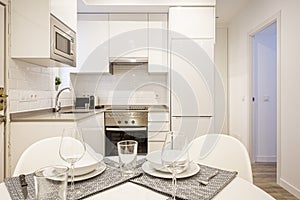 Living room with a round dining table with tableware set with crystal stemware and white crockery in an open plan kitchen with