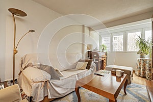 Living room with sofa covered with protective cloth, wooden coffee table and gazebo with white aluminum windows