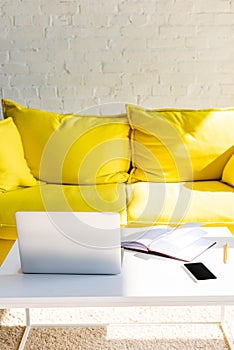 Living room with yellow sofa and table with laptop, smartphone and notepad