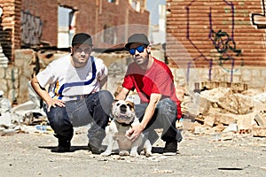 Living in a rough neighborhood. Two urban males kneeling down with a dog in their neighborhood.