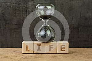 Living time for human life countdown, lifetime or retirement concept, sandglass or hourglass on wooden cube block with alphabet photo