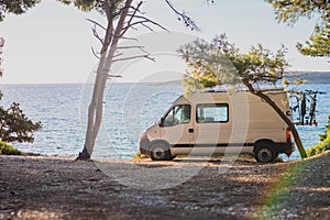 Living the vanlife. White van camper parked on the beach, nice trees around and blue sky just behind the van in the background.