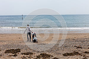 LLandudno, Wales, UK - MAY 27, 2018 Father with baby in baby carriage walking on the beach. Single parent with baby on the seashor