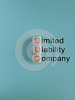 LLC - Limited Liability Company symbol. Orange words on wooden cubes on a blue background.