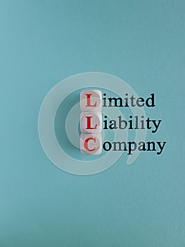 LLC - Limited Liability Company symbol. Red words on wooden cubes on a blue background.