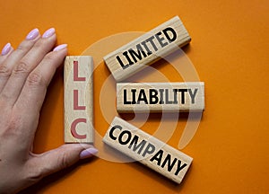 LLC - Limited liability company. Wooden cubes with word LLC. Businessman hand. Beautiful orange background. Business and LLC