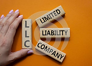 LLC - Limited liability company. Wooden cubes with word LLC. Businessman hand. Beautiful orange background. Business and LLC