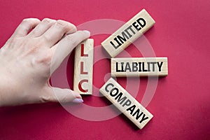 LLC - Limited liability company. Wooden cubes with word LLC. Businessman hand. Beautiful red background. Business and LLC concept