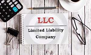 LLC Limited Liability Company is written in a white notepad near a calculator, coffee, glasses and a pen. Business concept