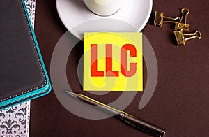 LLC Limited Liability Company written on yellow paper on a brown background near a coffee cup and diaries