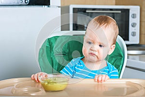 Llittle baby does not want to eat first complementary food. Disgruntled child at highchair