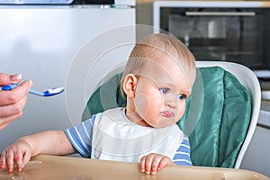 Llittle baby does not want to eat first complementary food. Disgruntled child at highchair