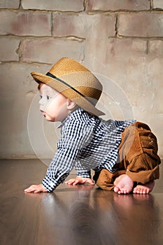 Llittle boy in retro hat and corduroy trousers learning to crawl on floor on all fours