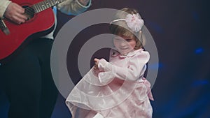 Llittle girl in vintage dress dances on stage, her father plays acoustic guitar
