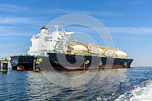 LNG tanker tied up to mooring posts in a harbour under blue sky