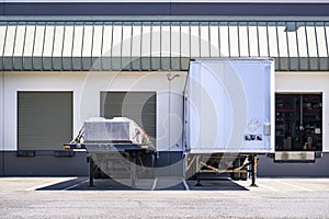 Loaded dry van and flat bed semi trailers without semi trucks unloading delivered cargo standing in warehouse dock gates