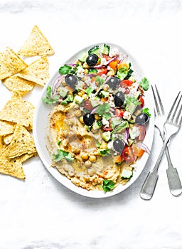 Loaded Greek salad hummus with corn tortilla chips on light background, top view. Delicious appetizer, tapas in a mediterranean