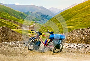 Loaded red touring bicycle with accessories stand in caucasus mountains with beautiful road panorama