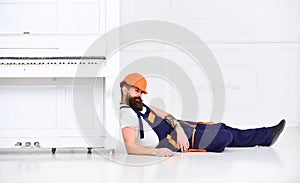 Loader lean on piano instrument. Man with beard, worker in overalls and helmet fall asleep tired, white background