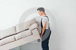 Loader moves sofa, couch. worker in overalls lifts up sofa, white background. Delivery service concept. Courier delivers furniture