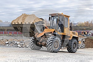 The loader is transporting sand or gravel in the front bucket. Heavy construction equipment at a construction site. Transportation