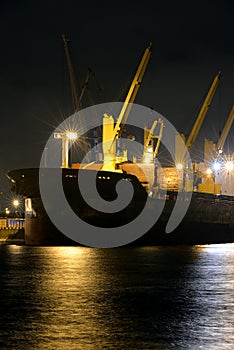 The loading cargo ship with cranes is moored in port at night