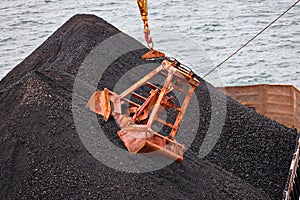 Loading coal from cargo barges onto a bulk carrier using ship cranes and grabs at the port of Muara Pantai, Indonesia. Close-up vi