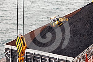 Loading coal from cargo barges onto a bulk carrier using ship cranes and grabs at the port of Muara Pantai, Indonesia. Close-up vi