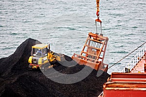 Loading coal from cargo barges onto a bulk carrier using ship cranes and grabs at the port of Muara Pantai, Indonesia. Close-up vi