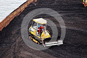 Loading coal from cargo barges onto a bulk carrier using ship cranes and grabs at the port of Muara Pantai, Indonesia. Close-up vi