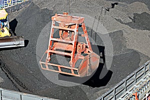 Loading coal from cargo barges onto a bulk carrier using ship cranes and grabs at the port of Muara Pantai, Indonesia. Close-up vi