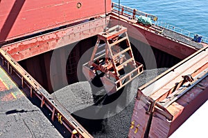 Loading coal from cargo barges onto a bulk carrier using ship cranes and grabs at the port of Muara Pantai, Indonesia. Close-up vi