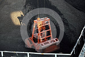 Loading coal from cargo barges onto a bulk carrier using ship cranes and grabs at the port of Muara Pantai, Indonesia. Close-up vi