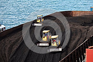 Loading coal from cargo barges onto a bulk carrier using ship cranes and grabs at the port of Muara Pantai, Indonesia. Close-up vi