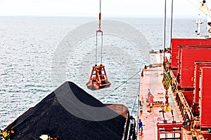 Loading coal from cargo barges onto a bulk carrier using ship cranes and grabs at the port of Muara Pantai, Indonesia. January,202